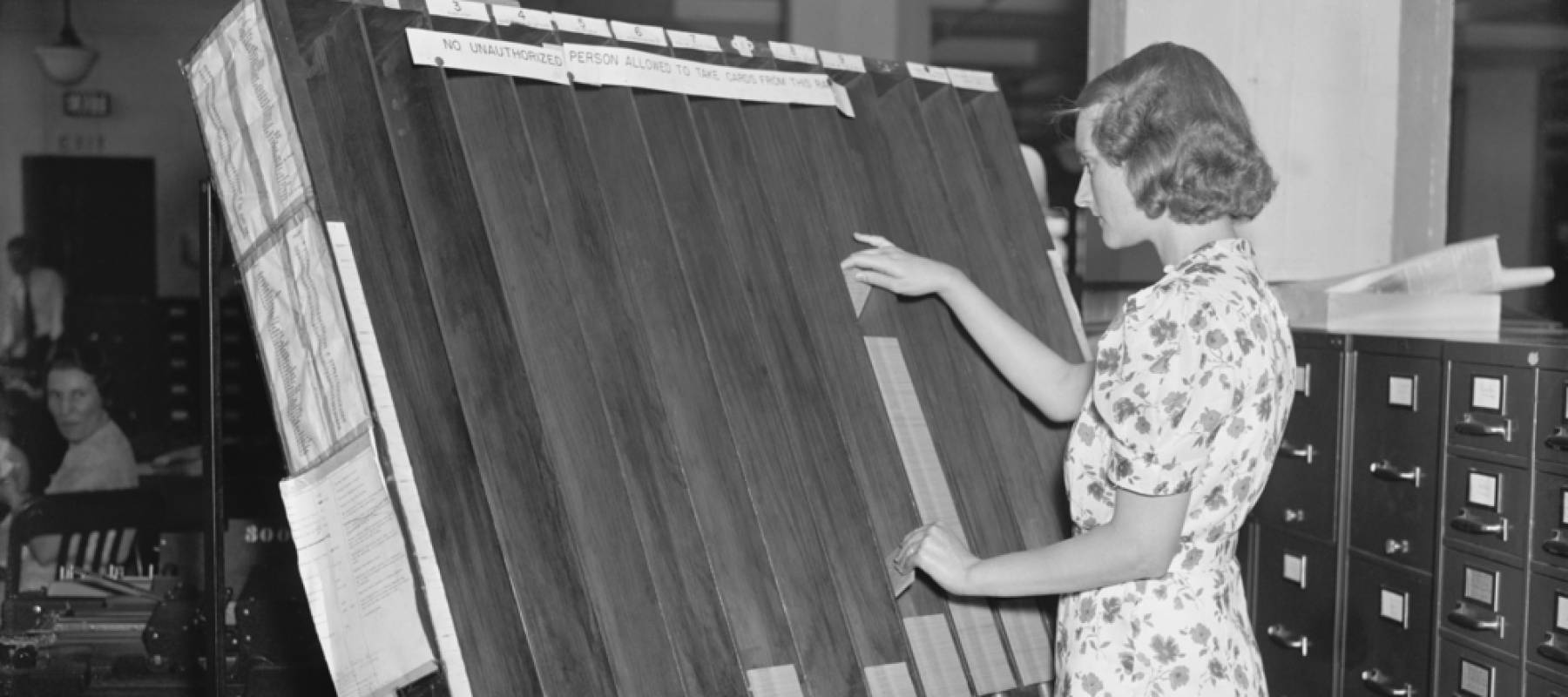 Black and white image of woman working in an office, moving something on a board in front of her.