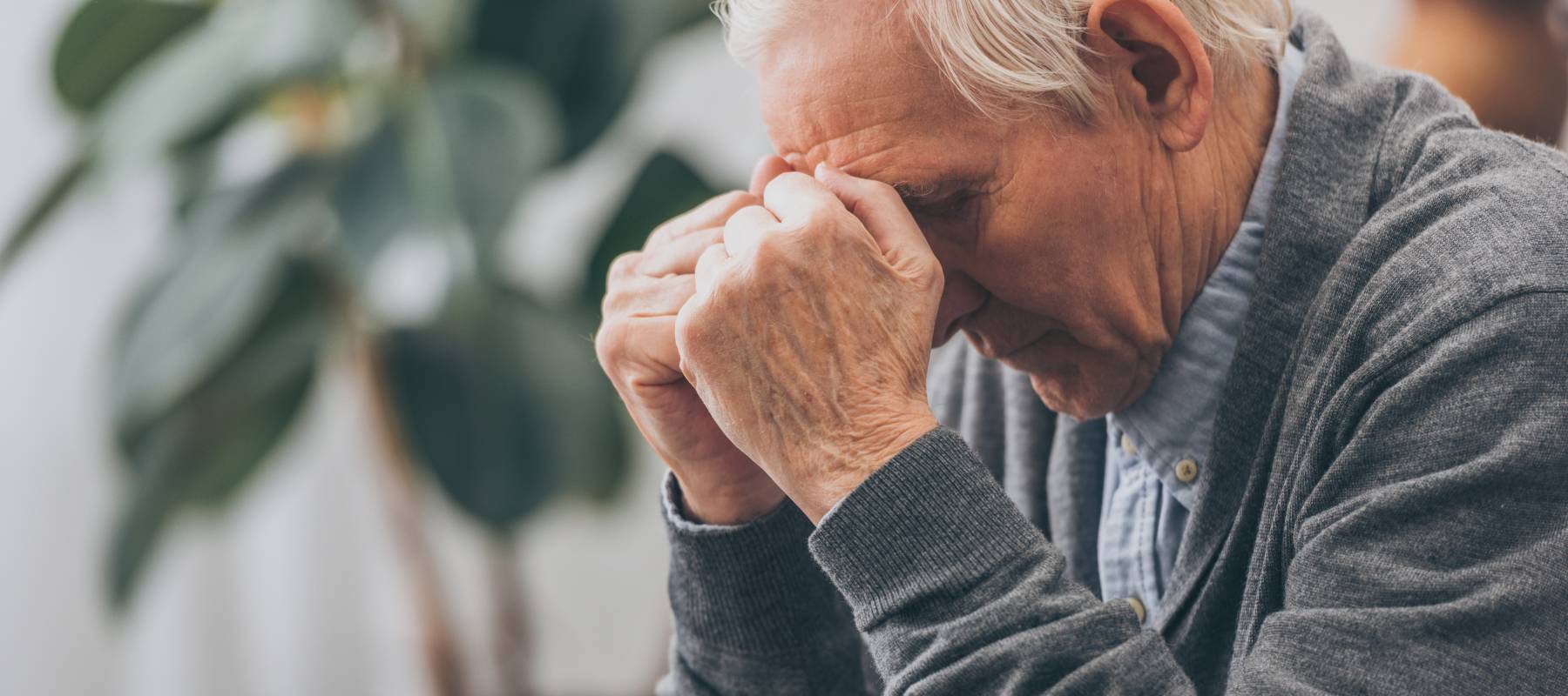 An older man holds his head while sitting.