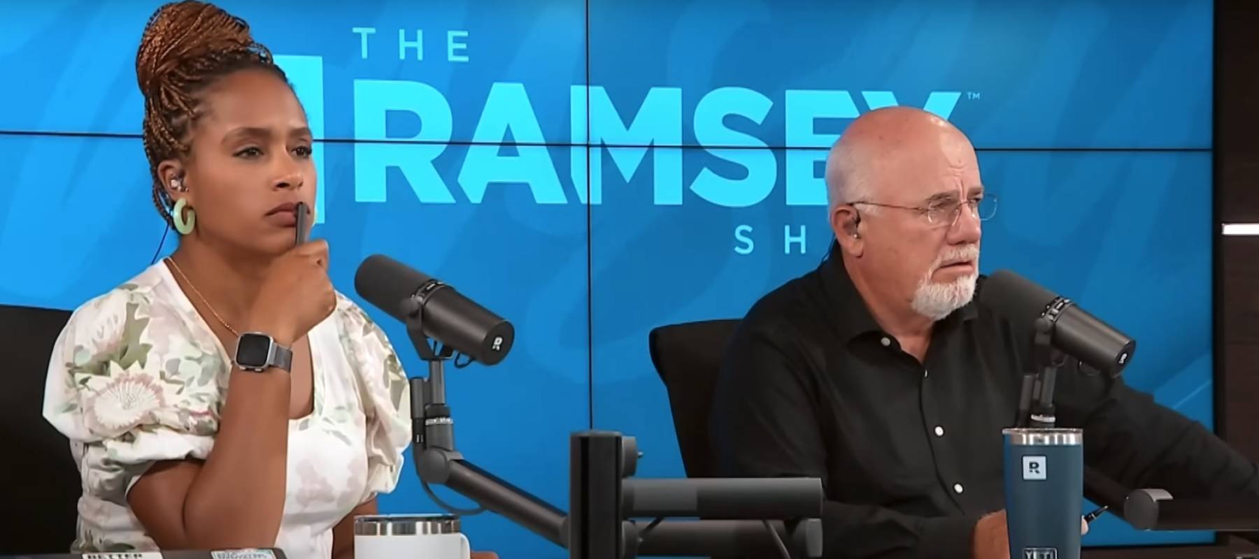 Hosts Dave Ramsey and Jade Warshaw look incredulous sitting in front of a microphone on the set of his radio show.