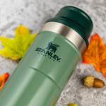 a green Stanley tumbler against an autumn background of fallen leaves