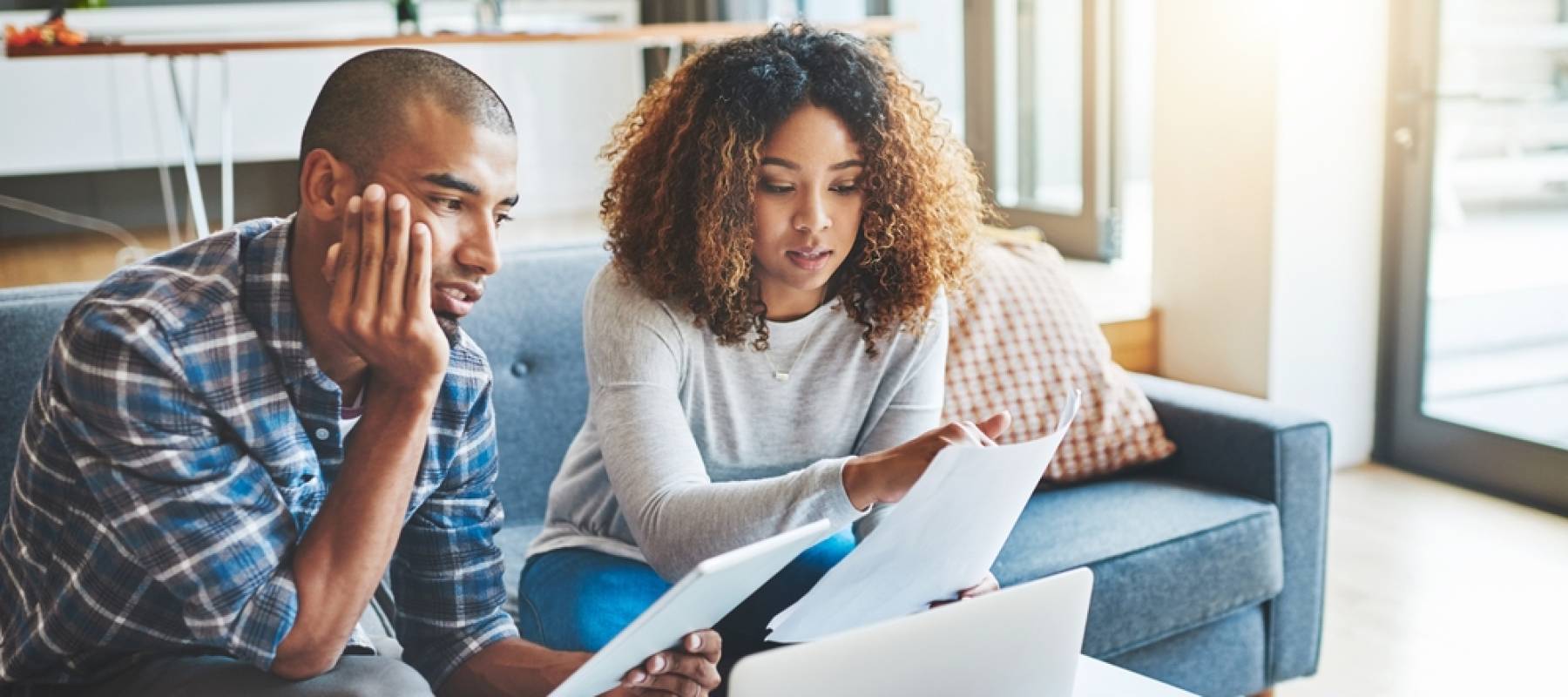 a young couple looking stressed about financial woes in front of a laptop at home