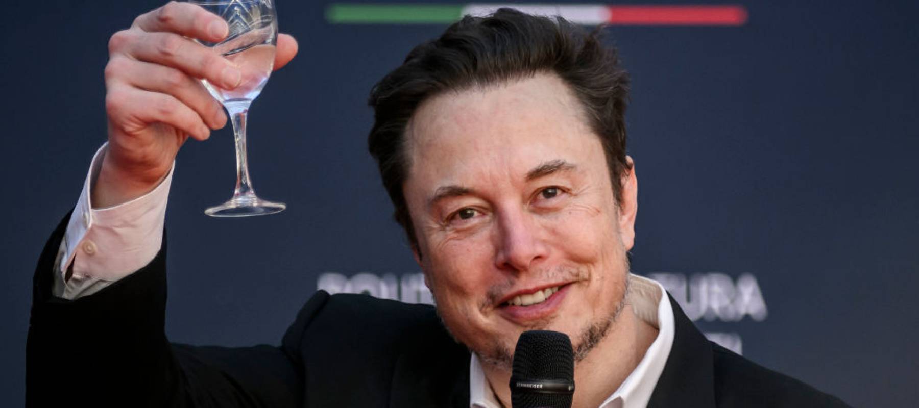 Elon Musk, chief executive officer of Tesla Inc and X (formerly Twitter) Ceo speaks at the Atreju political convention organized by Fratelli d'Italia, raising a glass in his hand.