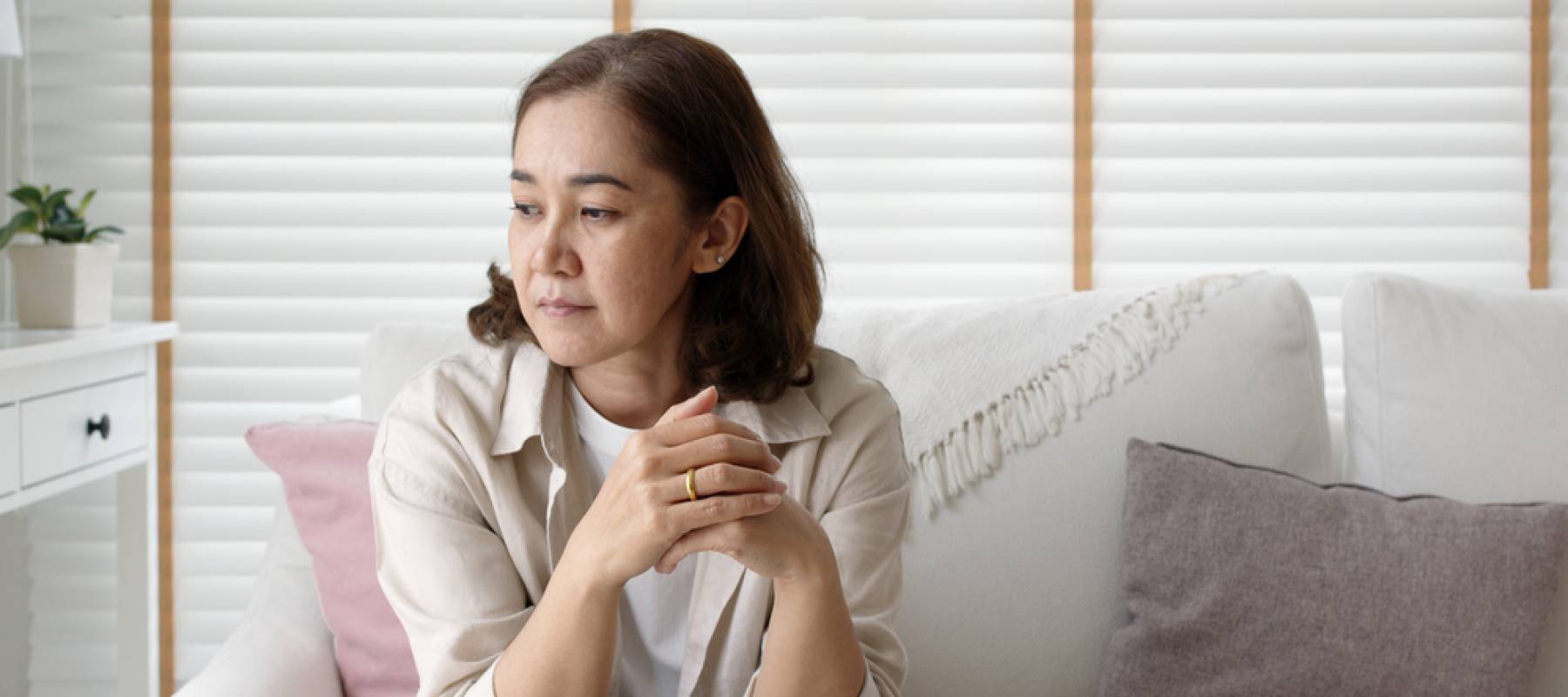 upset middle-aged Hispanic woman looking off to the side, sitting on a couch at home