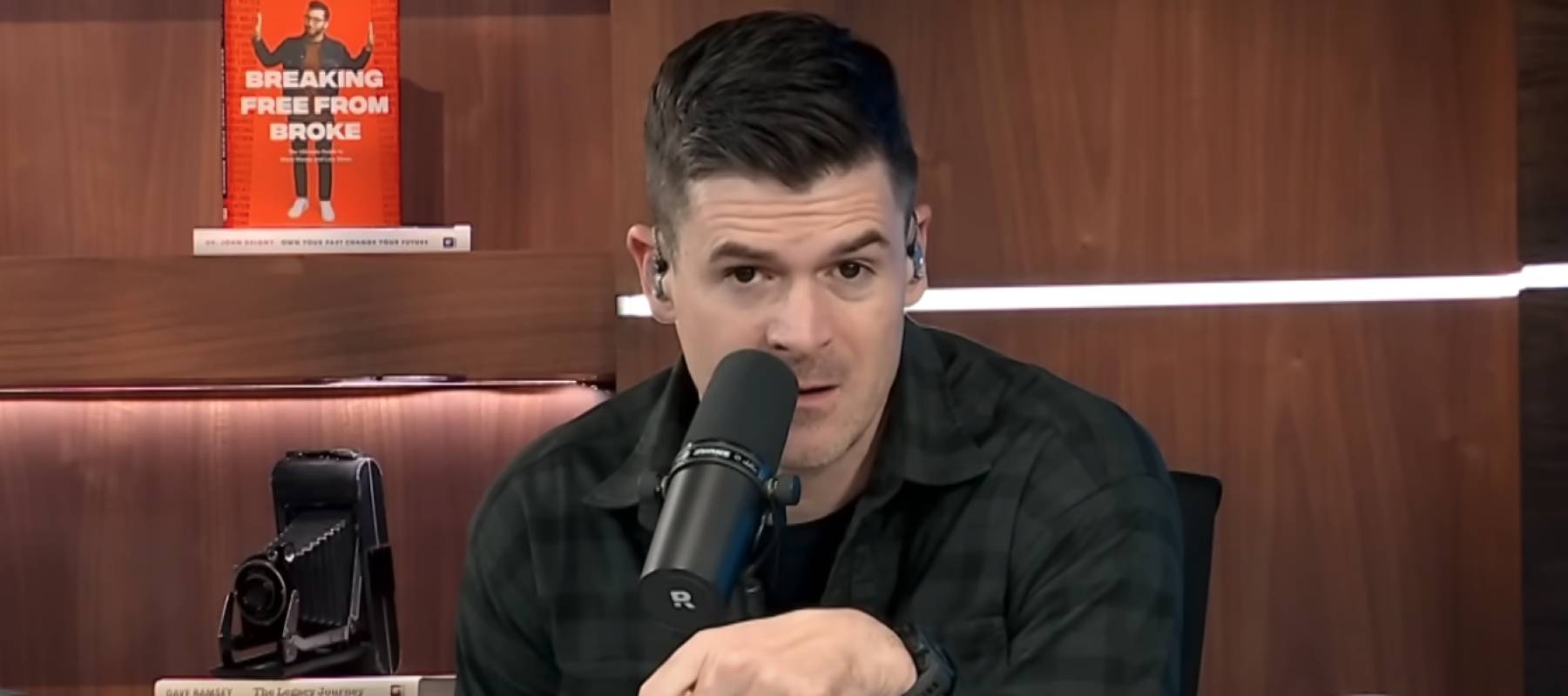 Man sitting in front of a microphone, making an incredulous look at the camera.