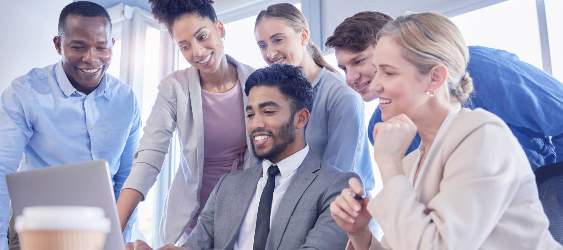 A business team gathers around a laptop.