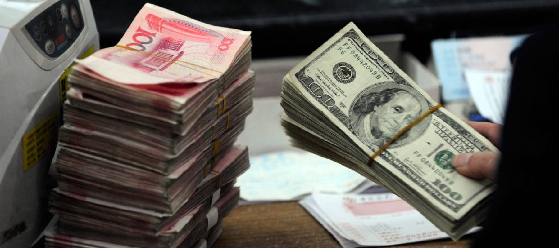 A Chinese bank worker prepares to count a stack of US dollars together with stacks of 100 Chinese yuan notes at a bank in Hefei, east China's Anhui province.