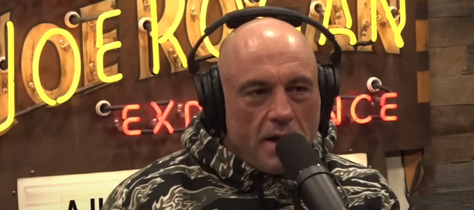 Joe Rogan seen on set of his podcast, speaking into microphone with headphones on.