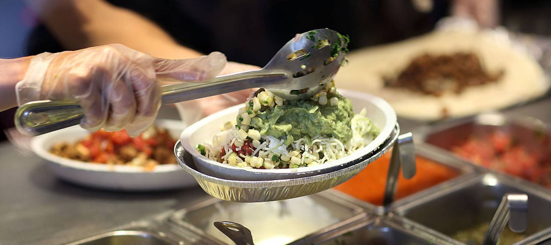 Chipotle worker scoops guacamole on top of a heaping bowl of food.