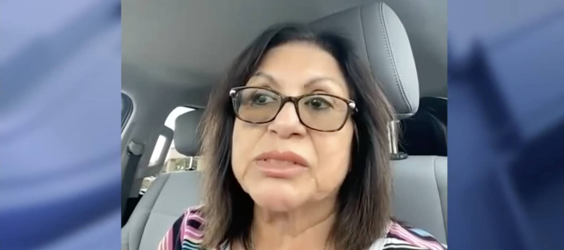 Woman with brown hair, sitting in car, speaking to camera but looking to the side.