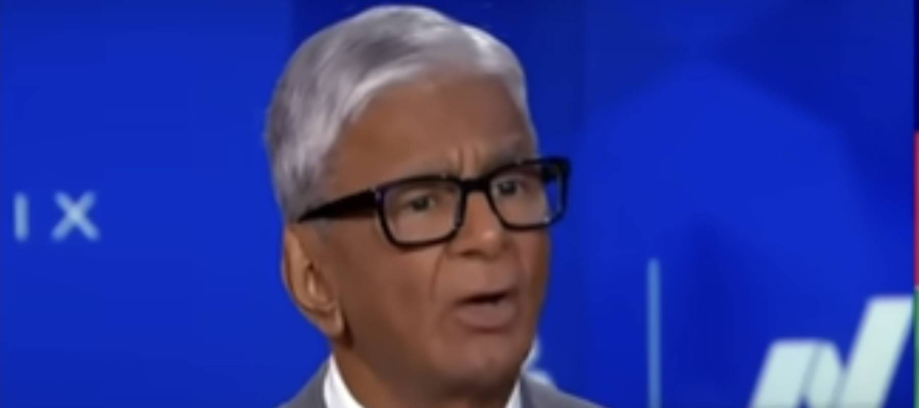 Man in suit seen speaking on television set.