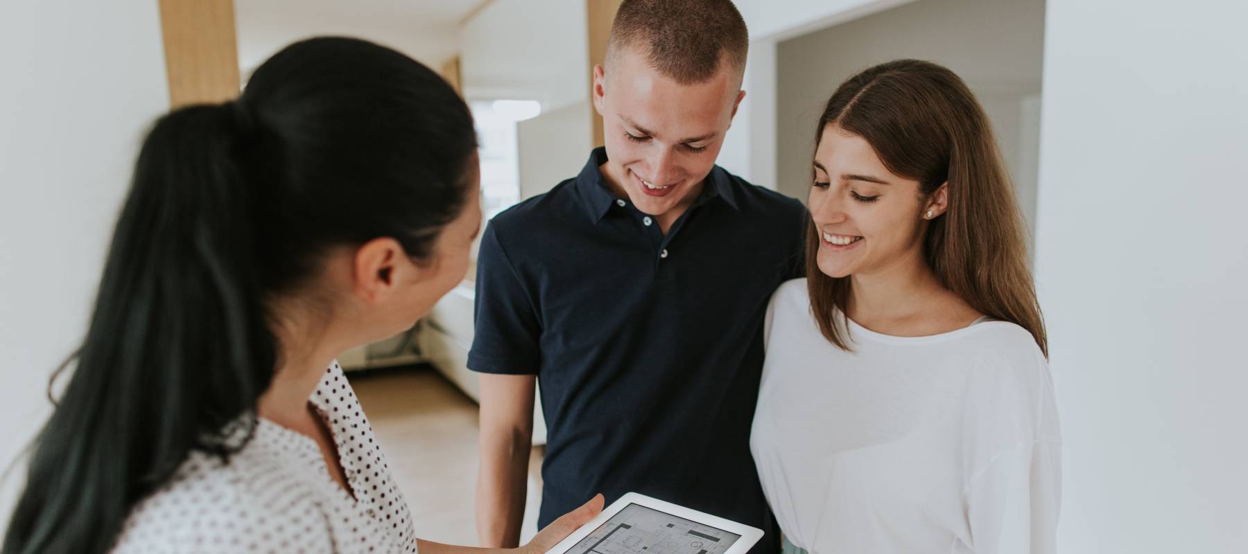 Female estate agent holding digital tablet and talking to young first time buyers in new apartment.