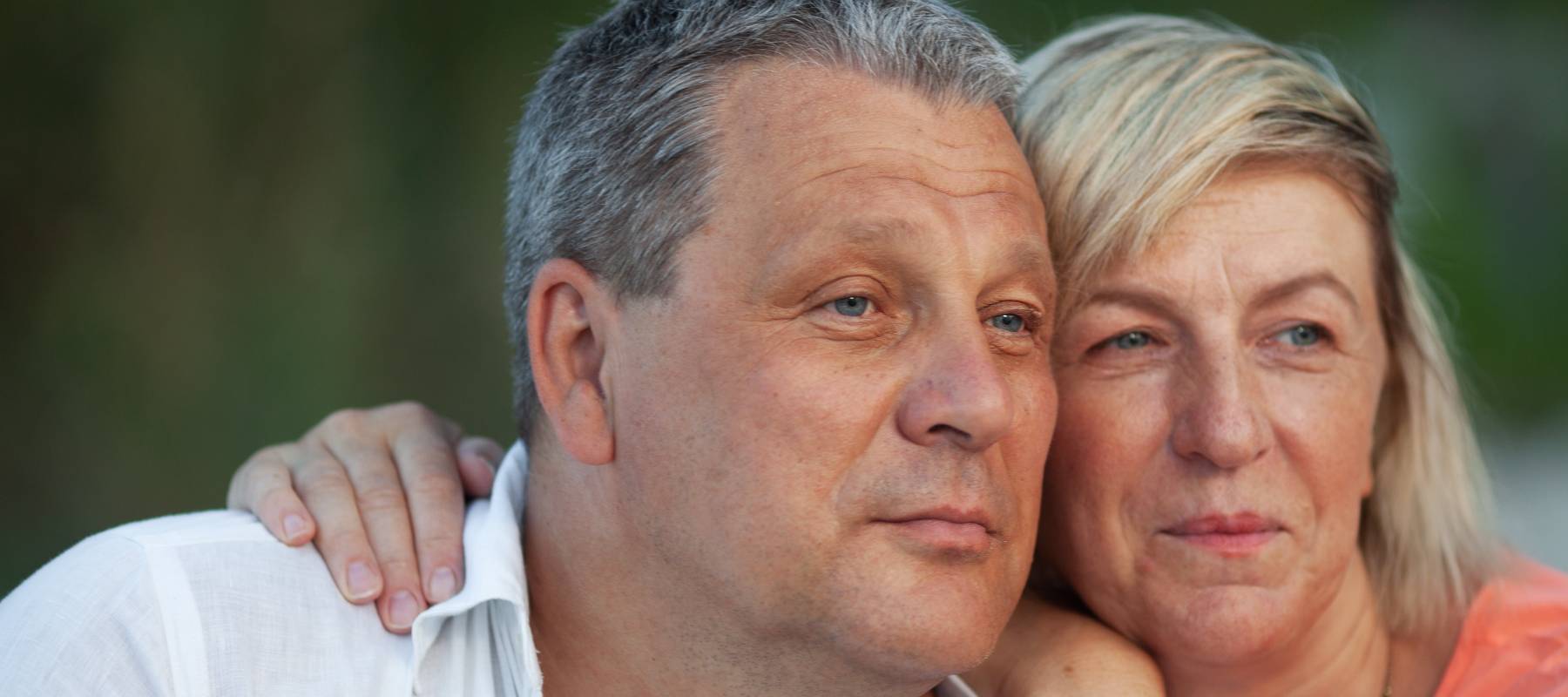 A man in a white shirt and a fair haired woman in an orange one are looking into the distance