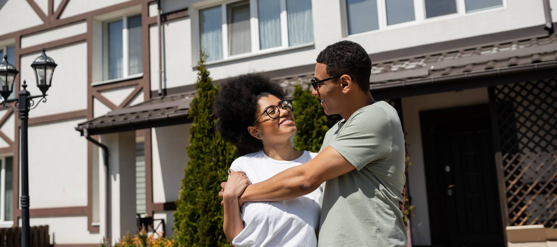 A young couple pose in front of a home.