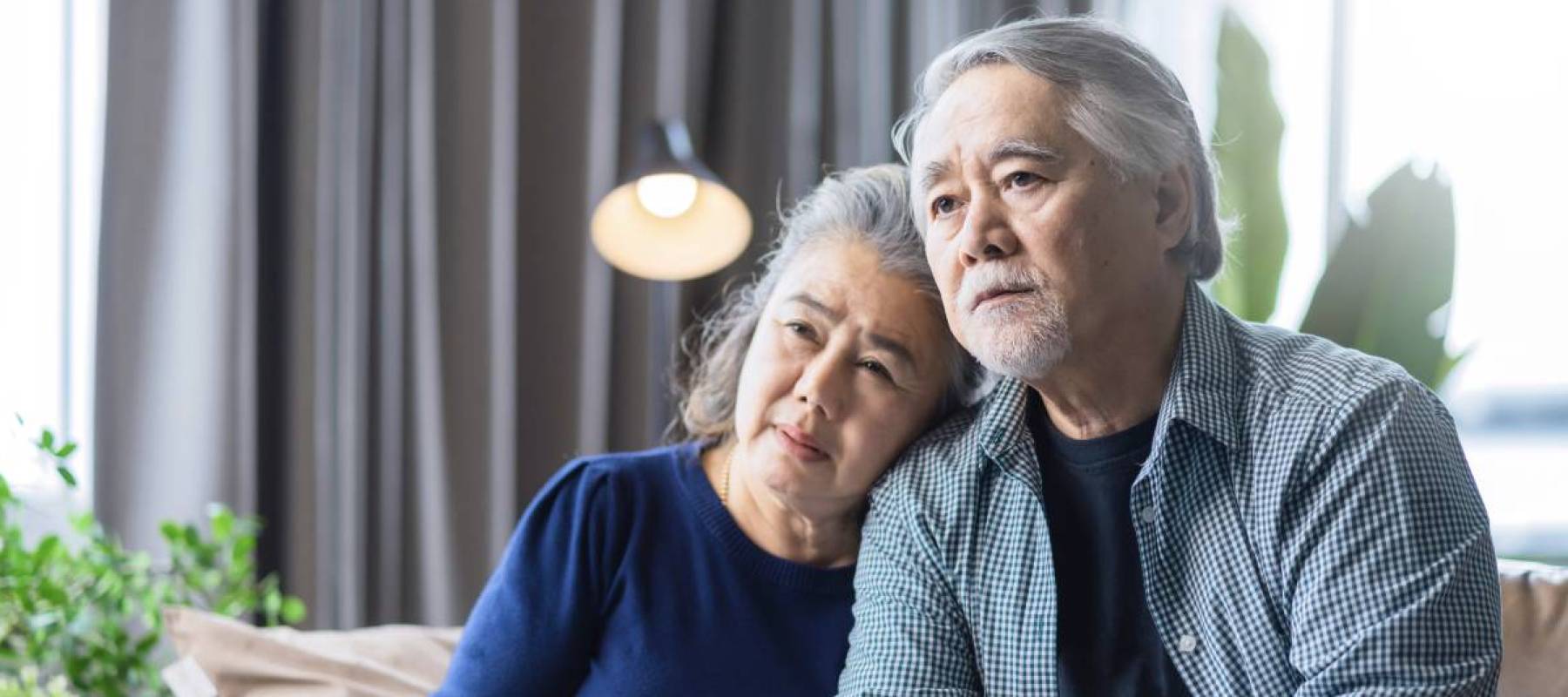 A retired couple looks pensive on a couch.