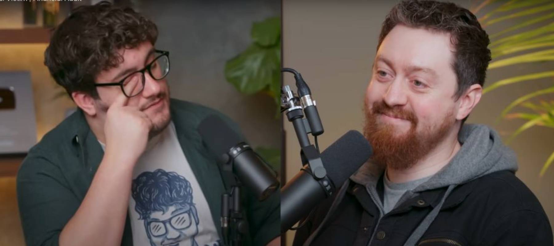 Two men seen facing each other talking into microphones, one rubbing his eye with his face looking frustrated and other smiling.