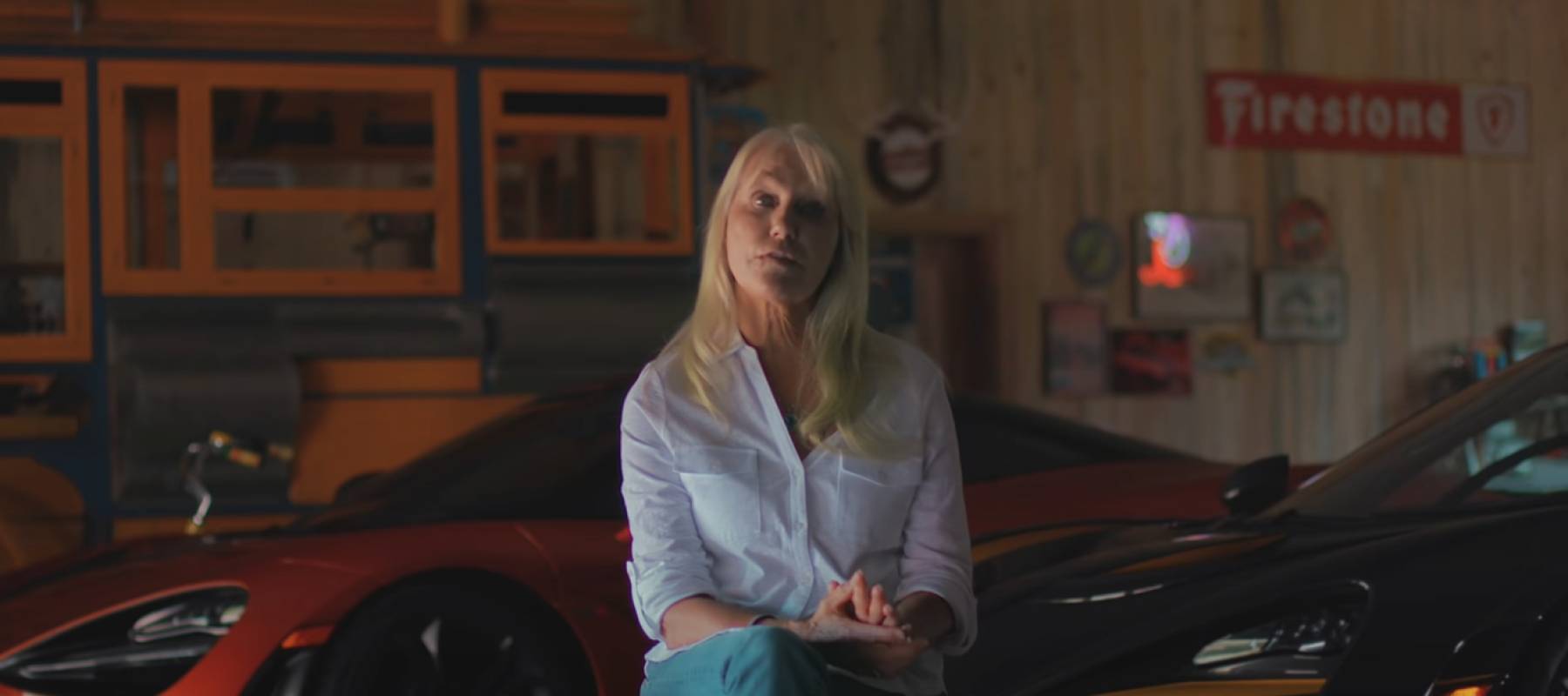 Woman seated on a chair in front of luxury cars behind her.