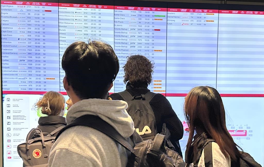 Travelers look at a departure information board at Pierre Elliott Trudeau International Airport in Montreal, Friday, Dec. 23, 2023. The authority overseeing the Montreal airport is rolling ou