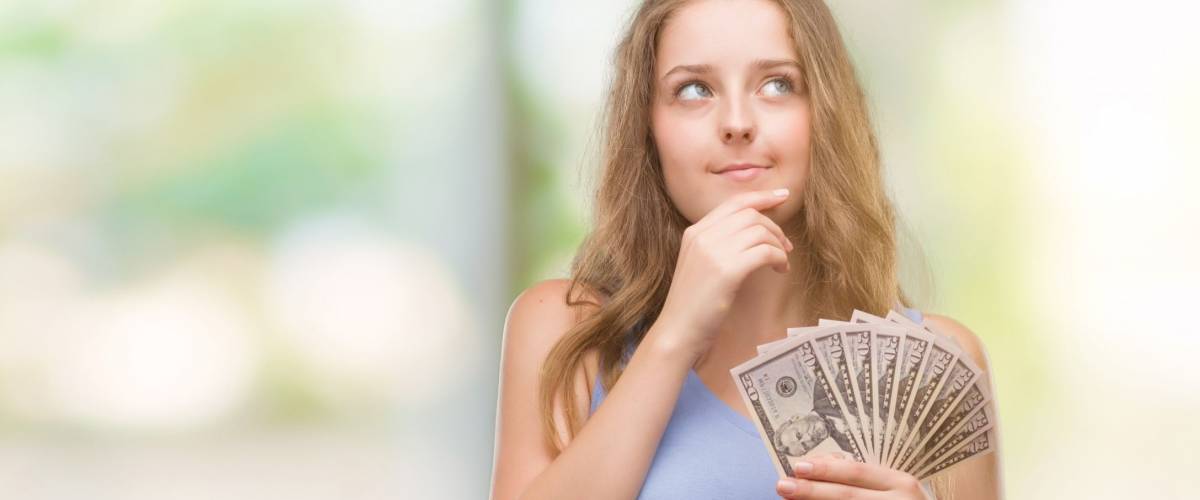 Young blonde woman holding dollars serious face thinking about question, very confused idea