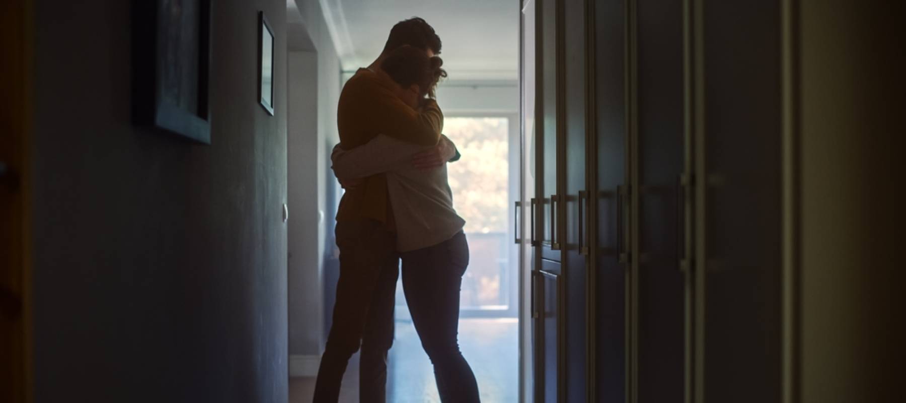 Sad couple embracing, comforting each other in hallway at home