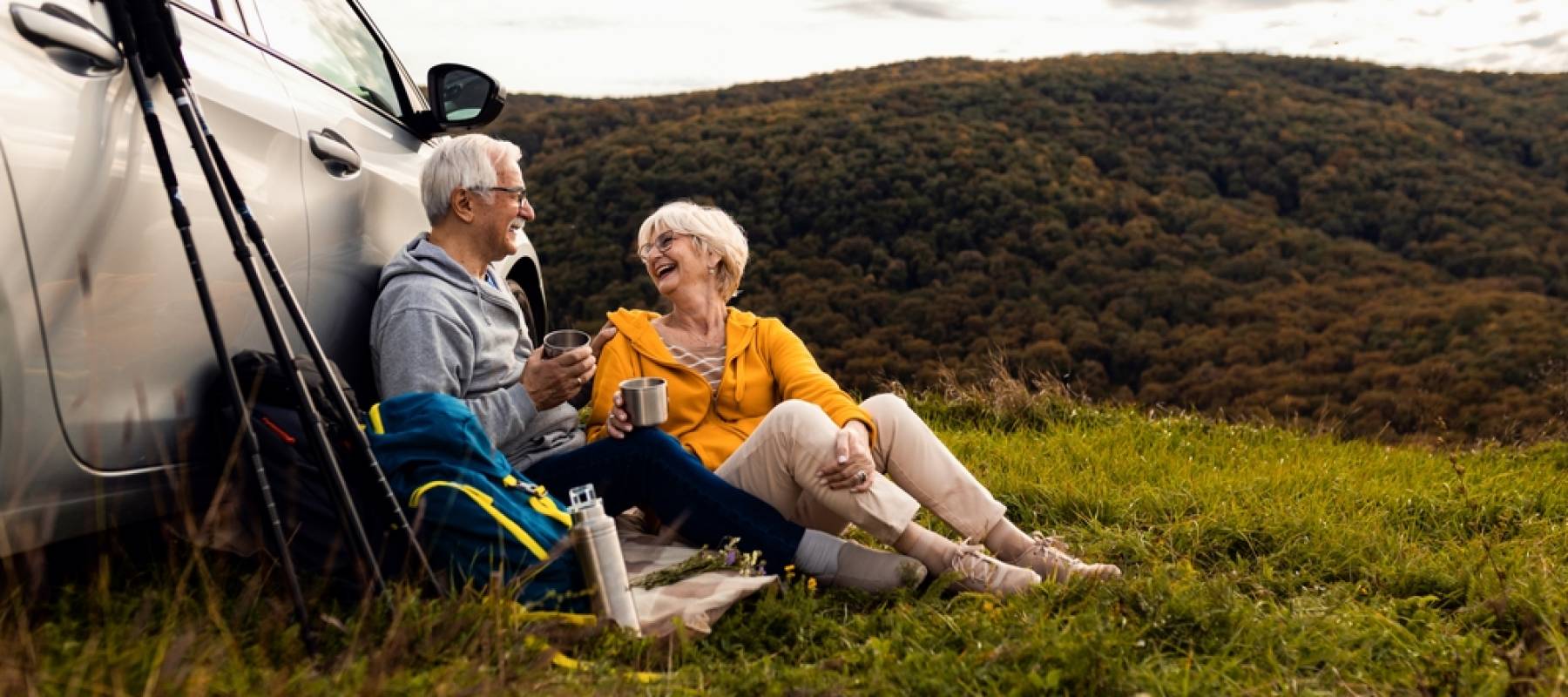 senior couple sitting against the car, resting after hiking in countryside