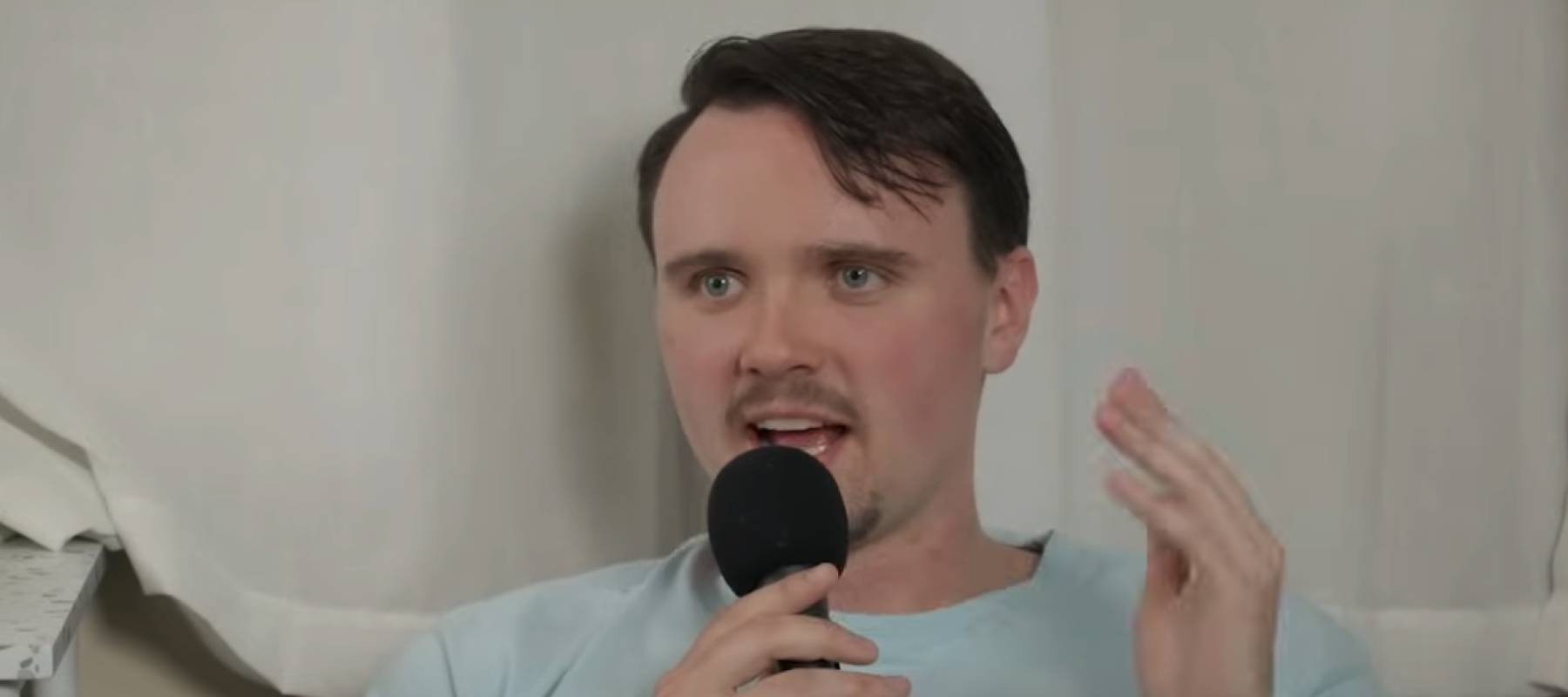 Young man speaking into microphone, sitting in living room.