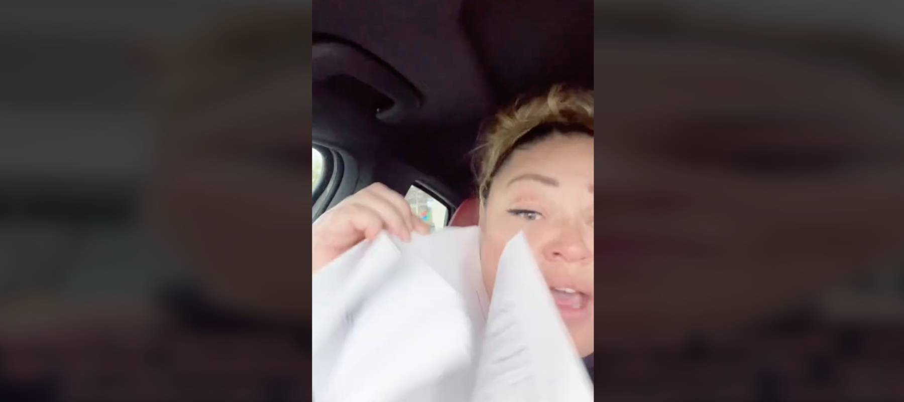 Woman in car looking at camera, holding up papers.