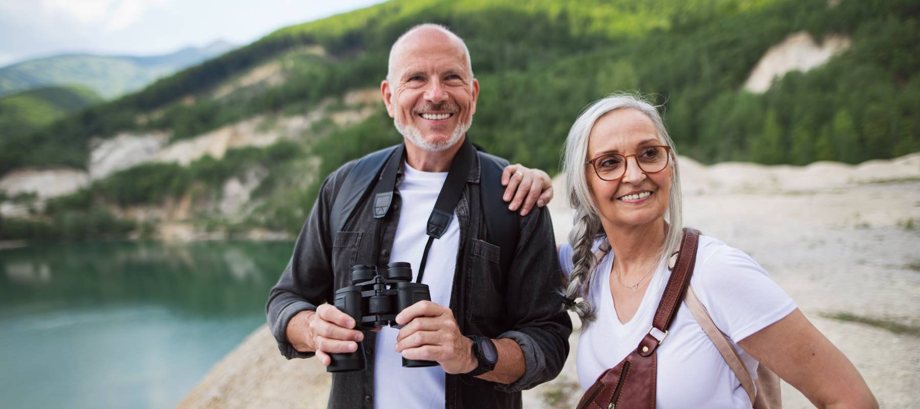 A happy senior couple on hiking trip on summer holiday, using binoculars.