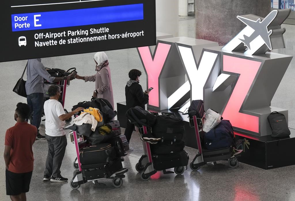 People wait with their luggage at Pearson International Airport in Toronto on Friday, August 5, 2022. A ruling from the Canadian Transportation Agency says that a couple who called to cancel 