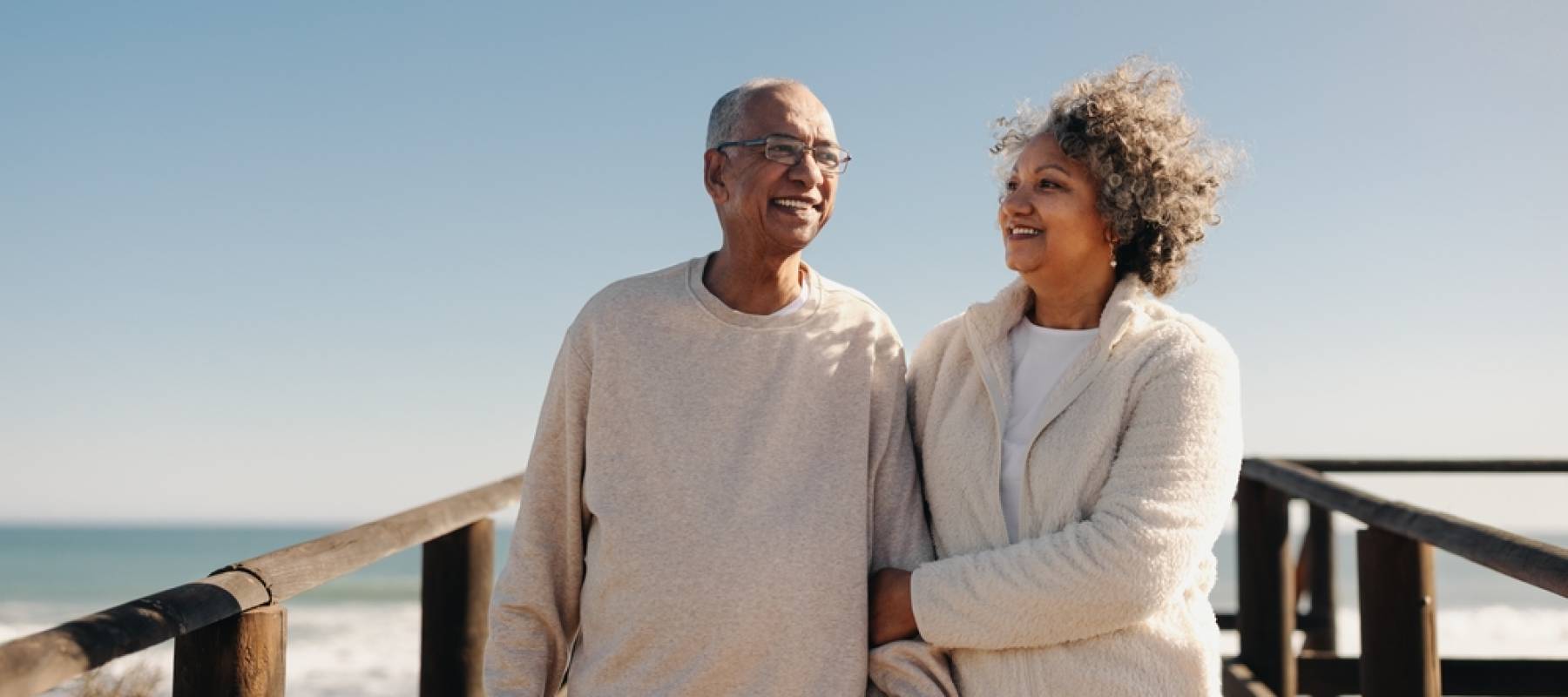 Black senior couple smiling happily while taking a walk along a wooden foot bridge at the beach
