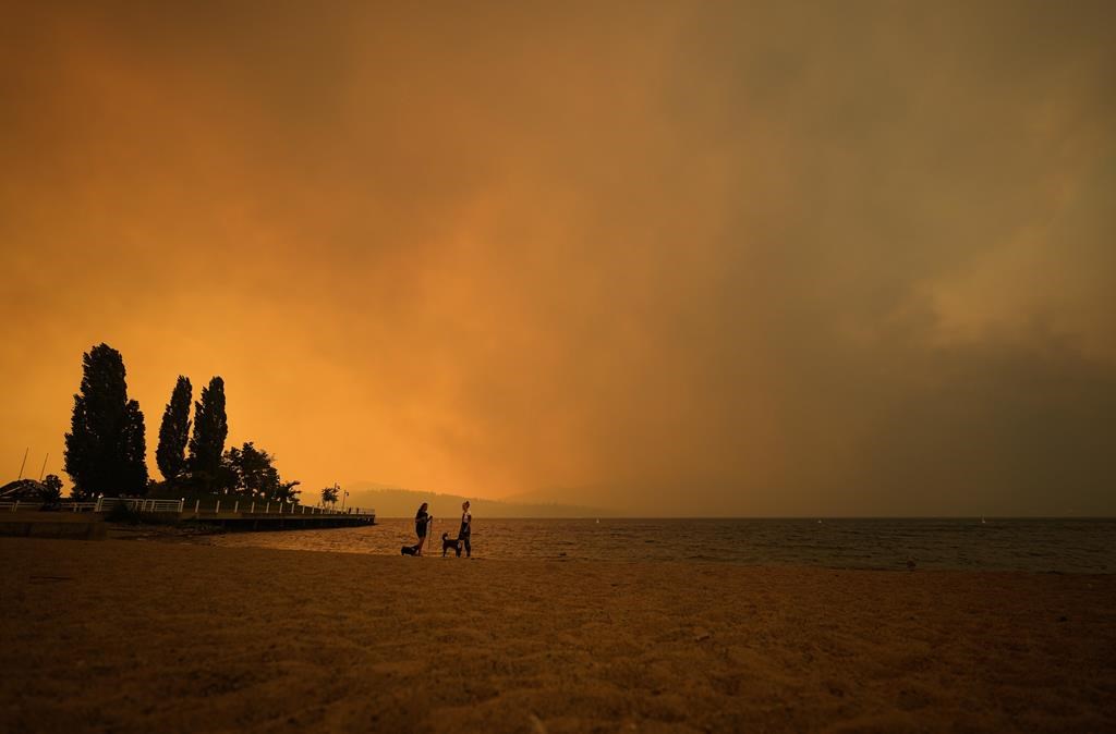 Smoke from the McDougall Creek wildfire fills the air and nearly blocks out the sun as people take in the view of Okanagan Lake from Tugboat Beach, in Kelowna, B.C., on August 18, 2023. 