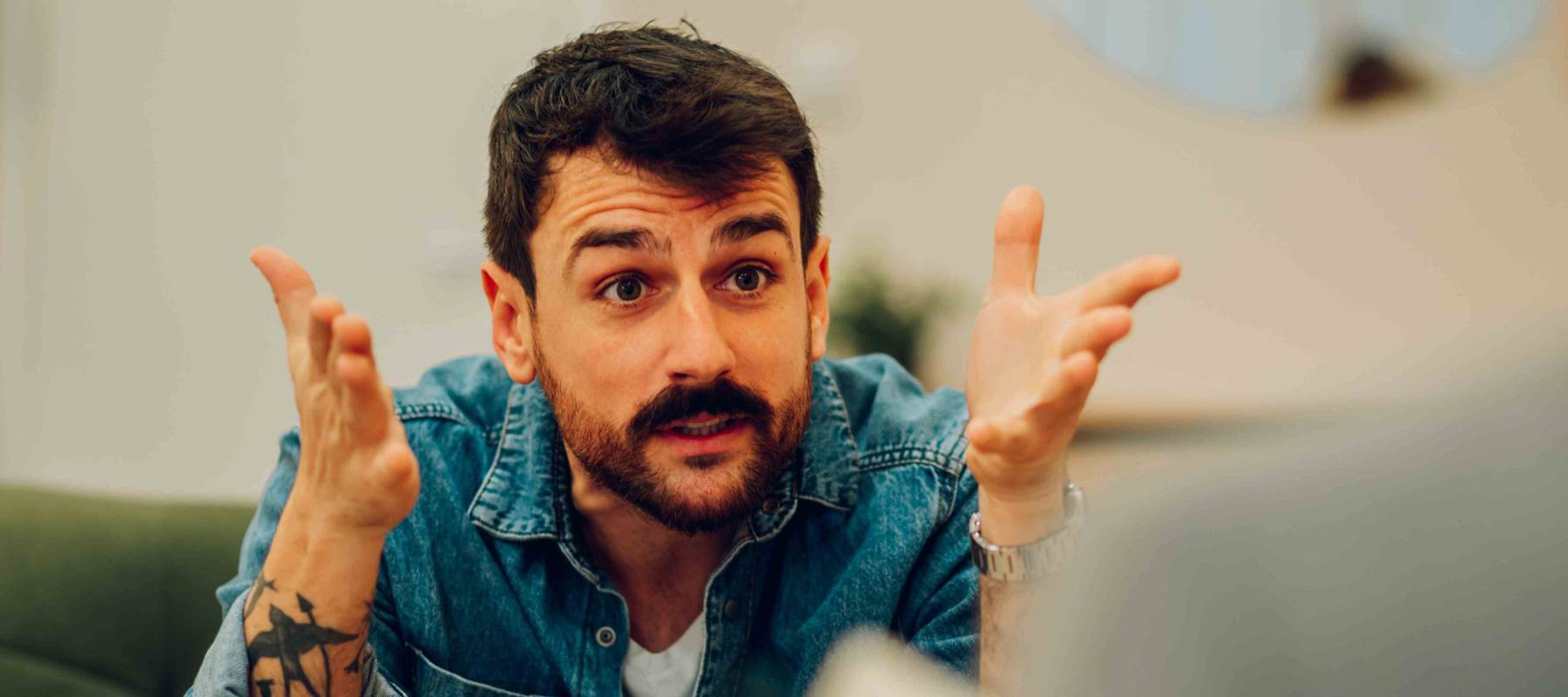 Man sitting on couch gestures intensely, looking upset.