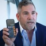 Grant Cardone sits in an office, holding up a calculator on his phone for the camera.