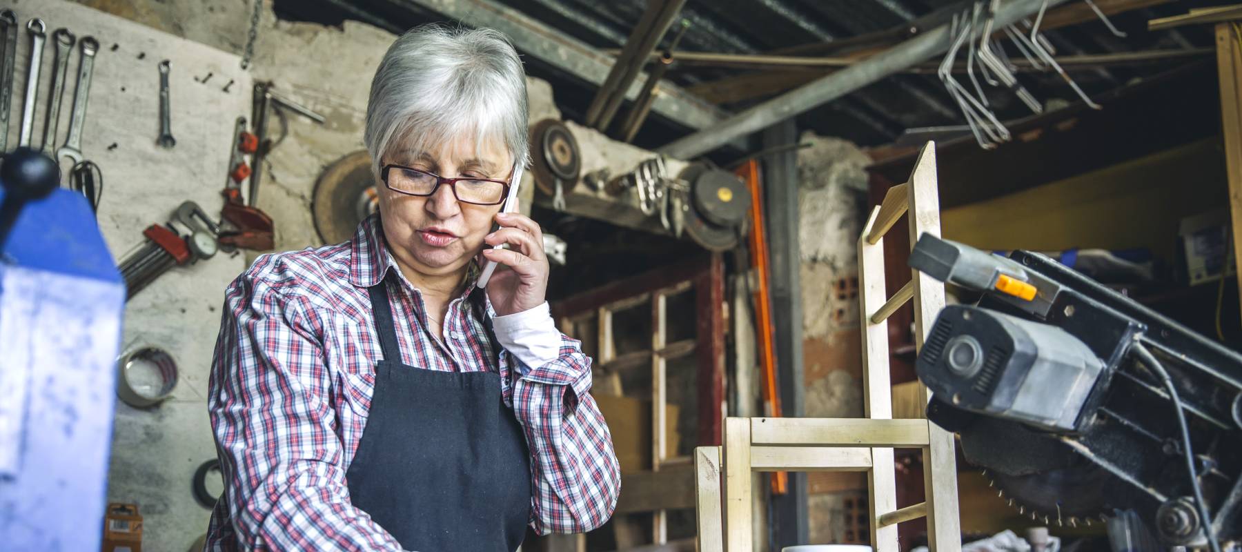 Senior female carpenter talking on the phone in her workshop.