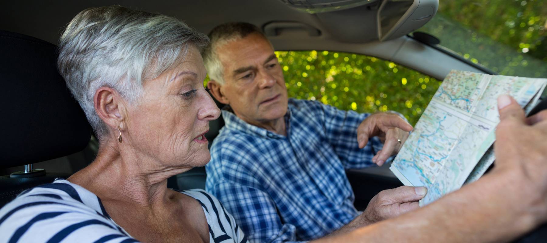 Senior couple sitting in a car, looking at a map.