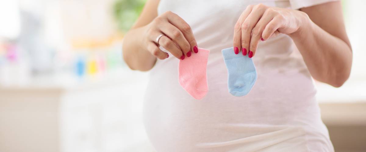 Pregnant woman holding one blue sock and one pink sock