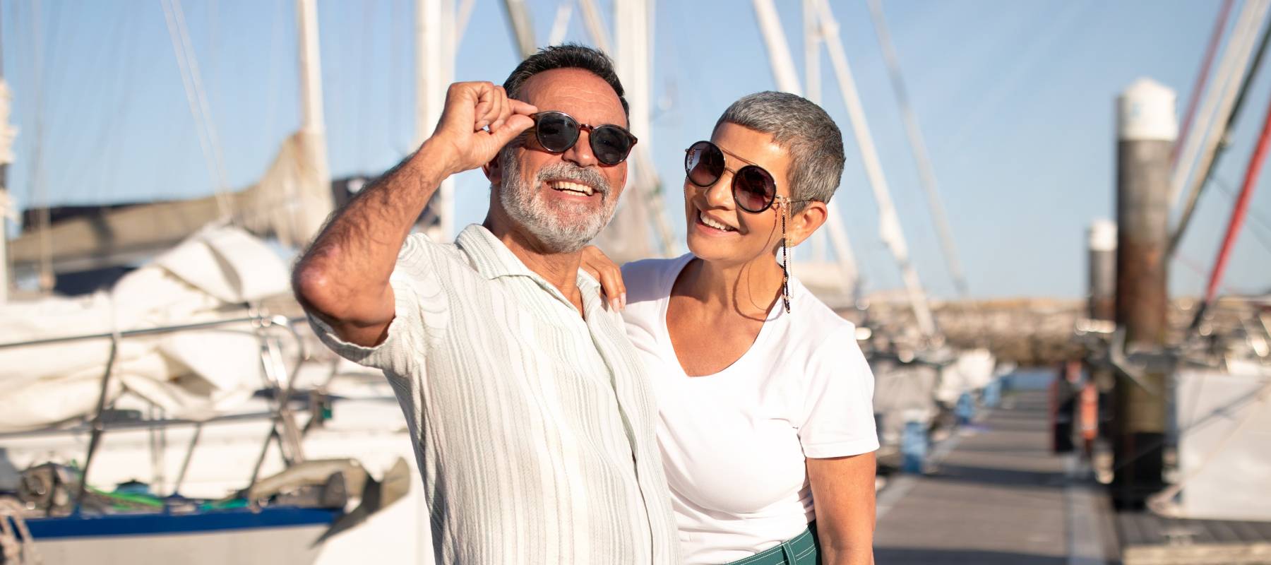 Happy older couple pose for a photo in front of boats at a marina.