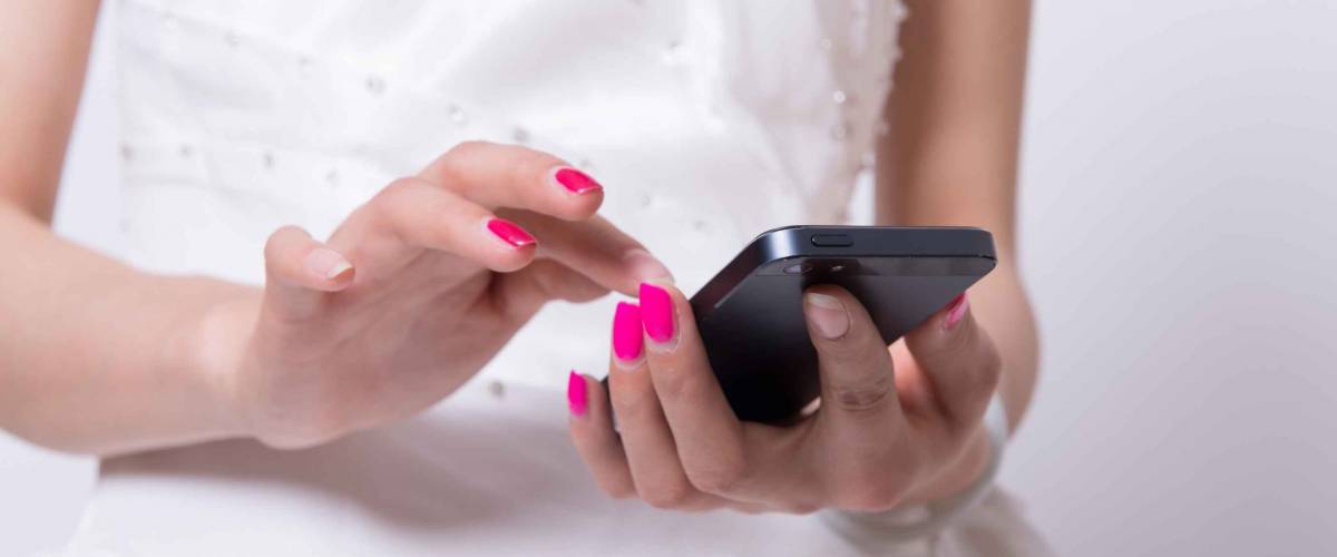 Close up of girl in wedding dress with pink nails texting on her mobile phone