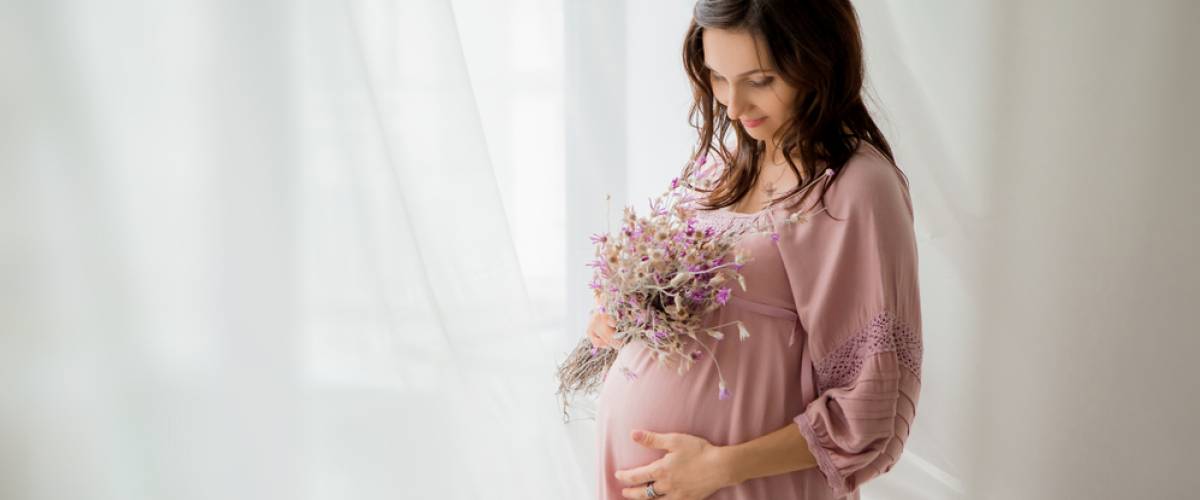 Pregnant woman in pink dress holding flowers