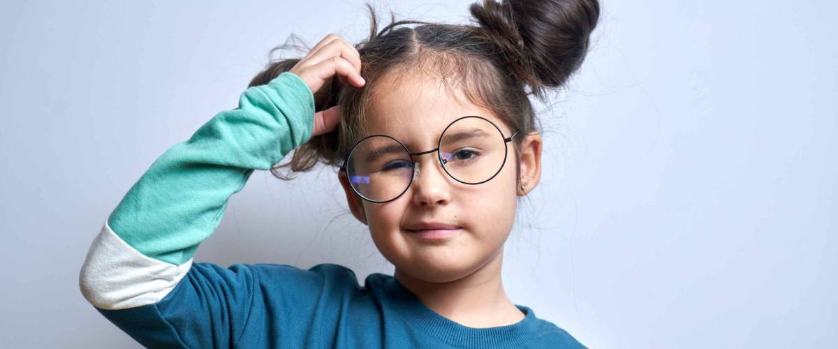 Funny little girl in glasses scratching her head doubts, makes decision isolated on yellow studio background