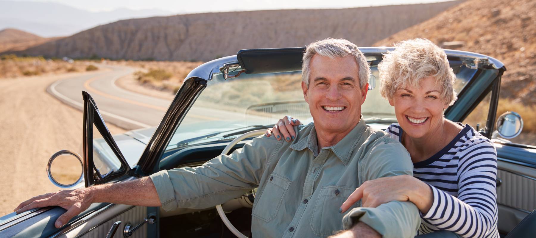Senior couple smile to camera from open top car, close up.