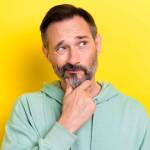 Portrait photo of old retired middle mature age man touch chin pouted lips look empty space choose product isolated on yellow color background