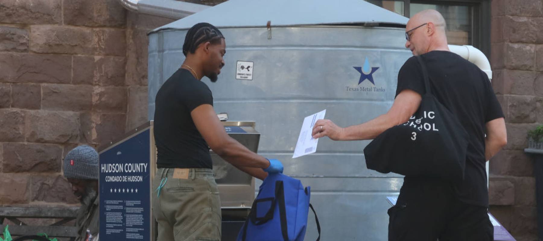 A man hands a mail-in ballot for the New Jersey primary election to a poll worker collecting ballots from a drop box.