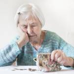 elderly 96 years old woman sitting at table at home and counting remaining coins from pension in her wallet