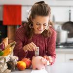 Portrait of happy young housewife putting money into piggy bank after shopping on local market