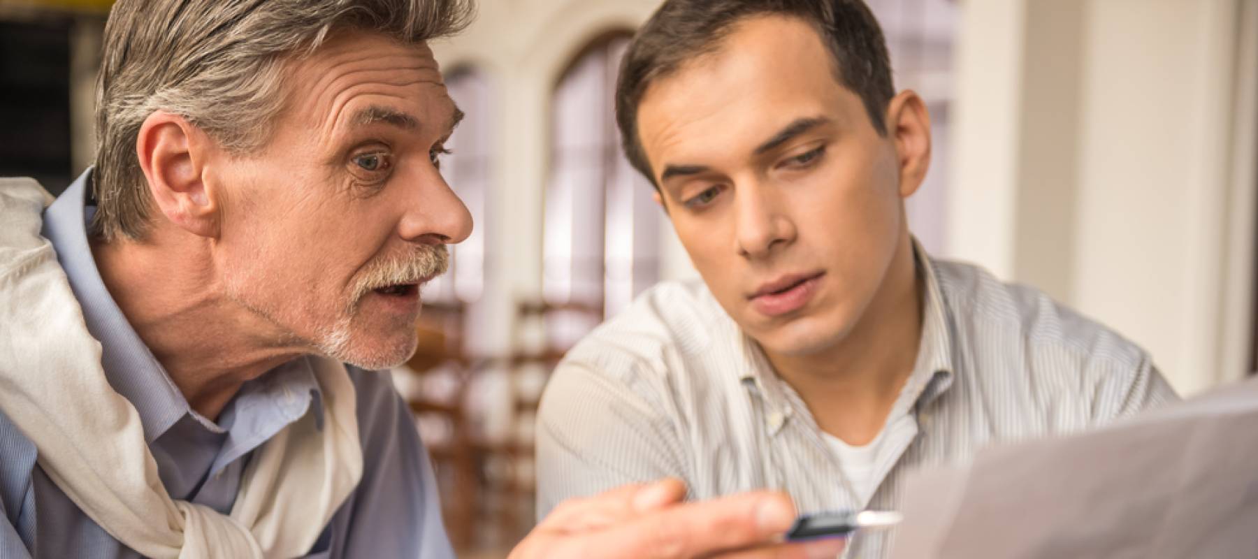 Two handsome businessmen in shirts sitting at the wooden table in urban cafe and working on project.