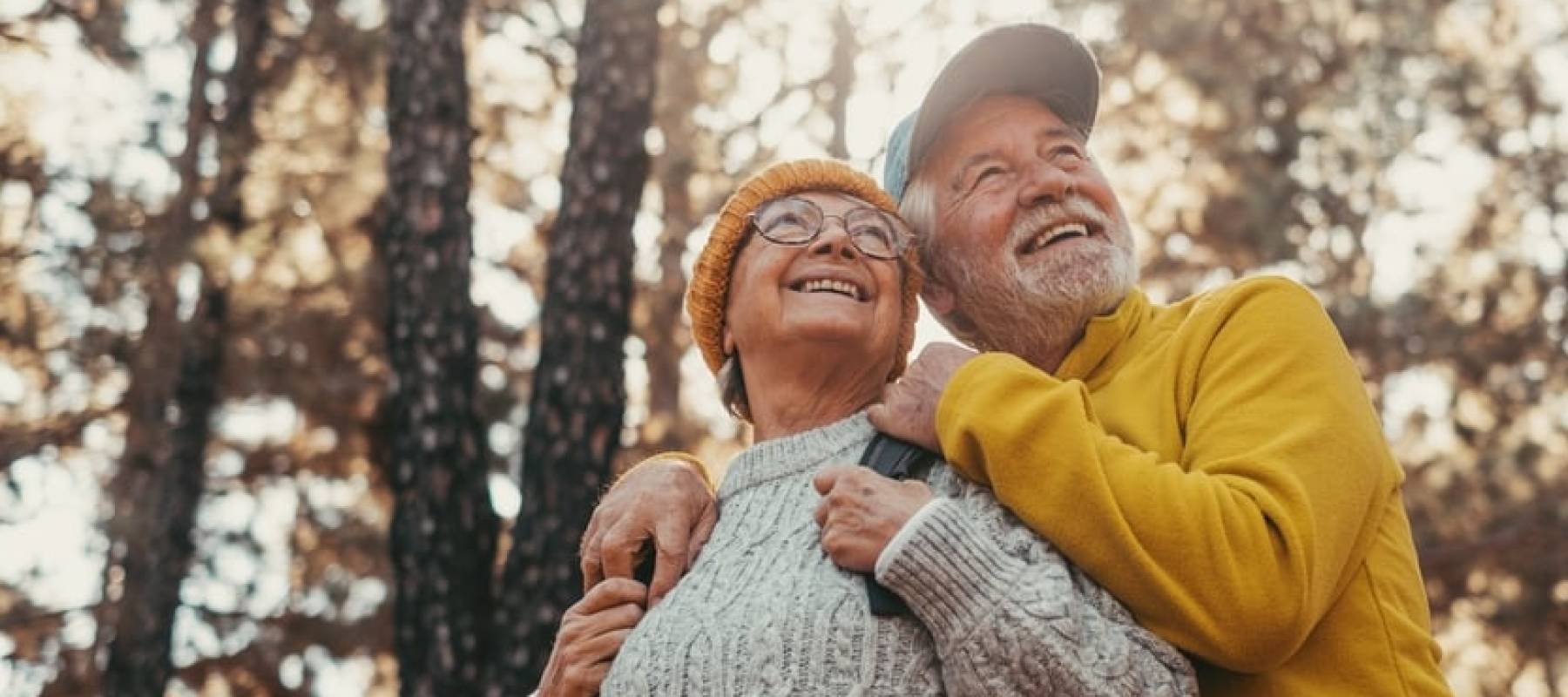 Couple hiking in the woods together, looking off to the side and smiling.