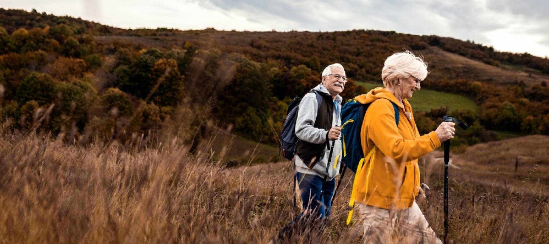 senior couple with backpacks hiking together in nature on autumn day