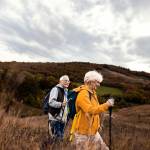 senior couple with backpacks hiking together in nature on autumn day