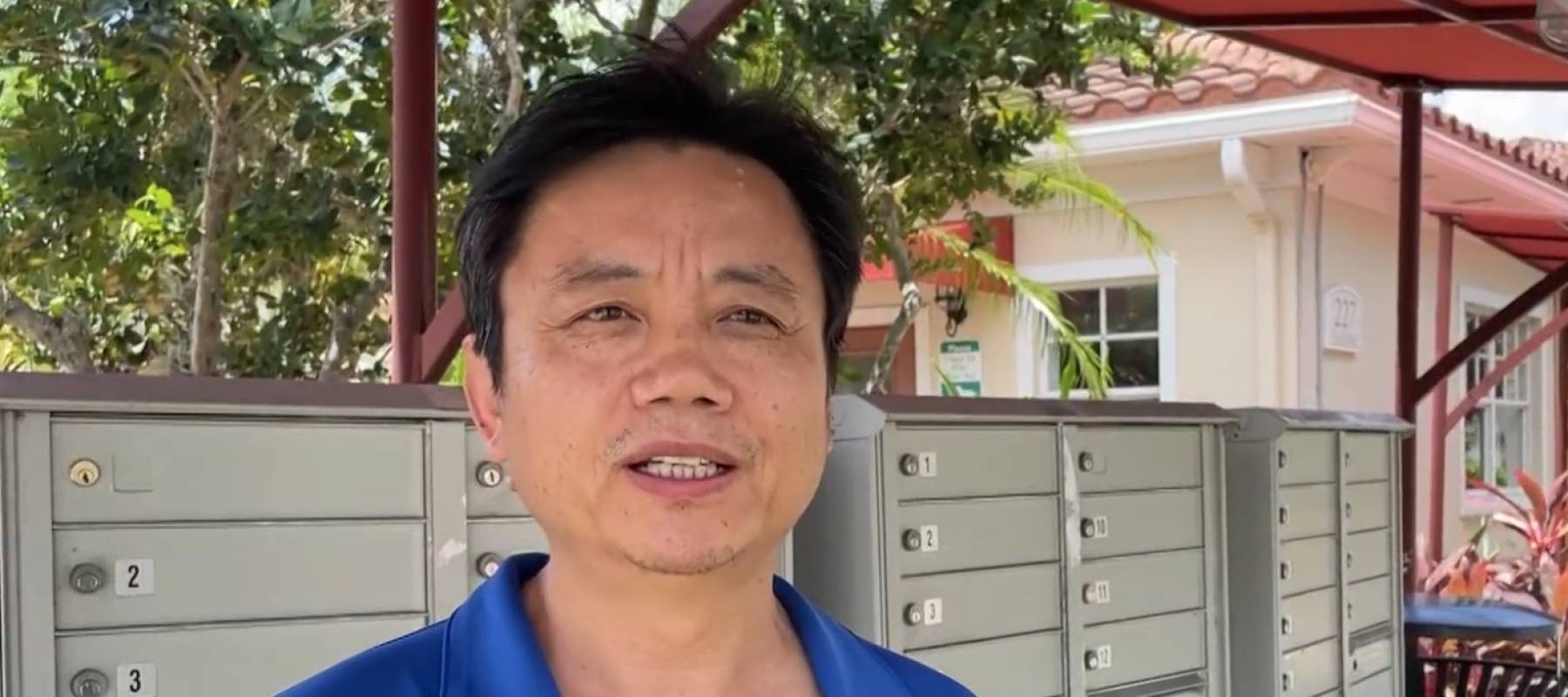 Man seen speaking to camera in front of condo mailbox.