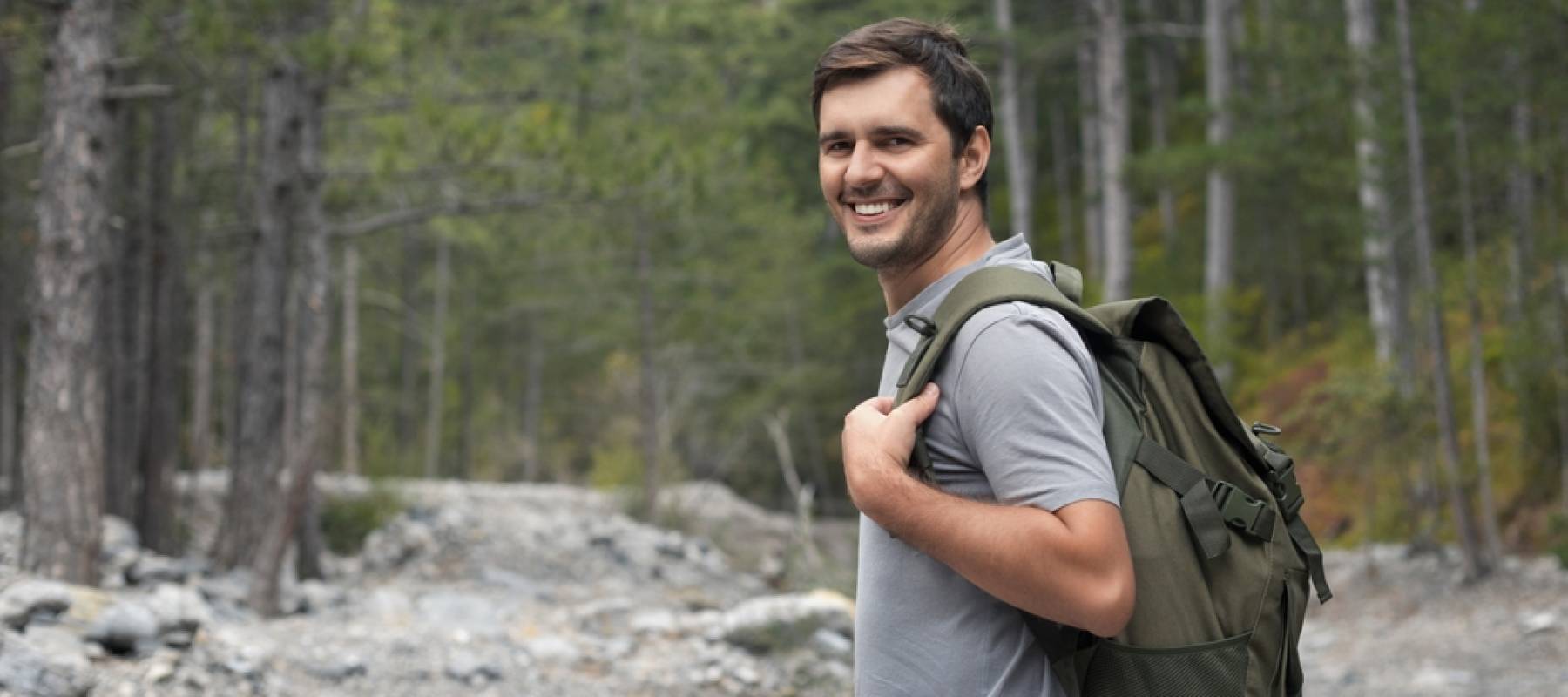 Portrait of happy smiling tourist man 30-35 years old with backpack hiking in national park